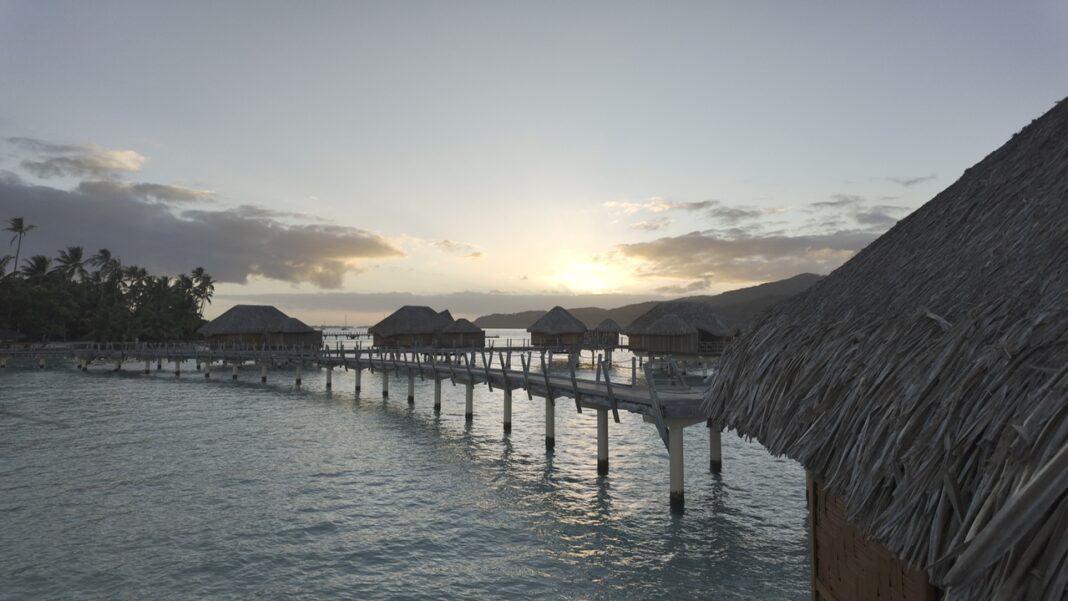 Sunrise at the Le Taha'a resort in French Polynesia. The sun is rising over the overwater bungalows with scattered clouds in the distance.